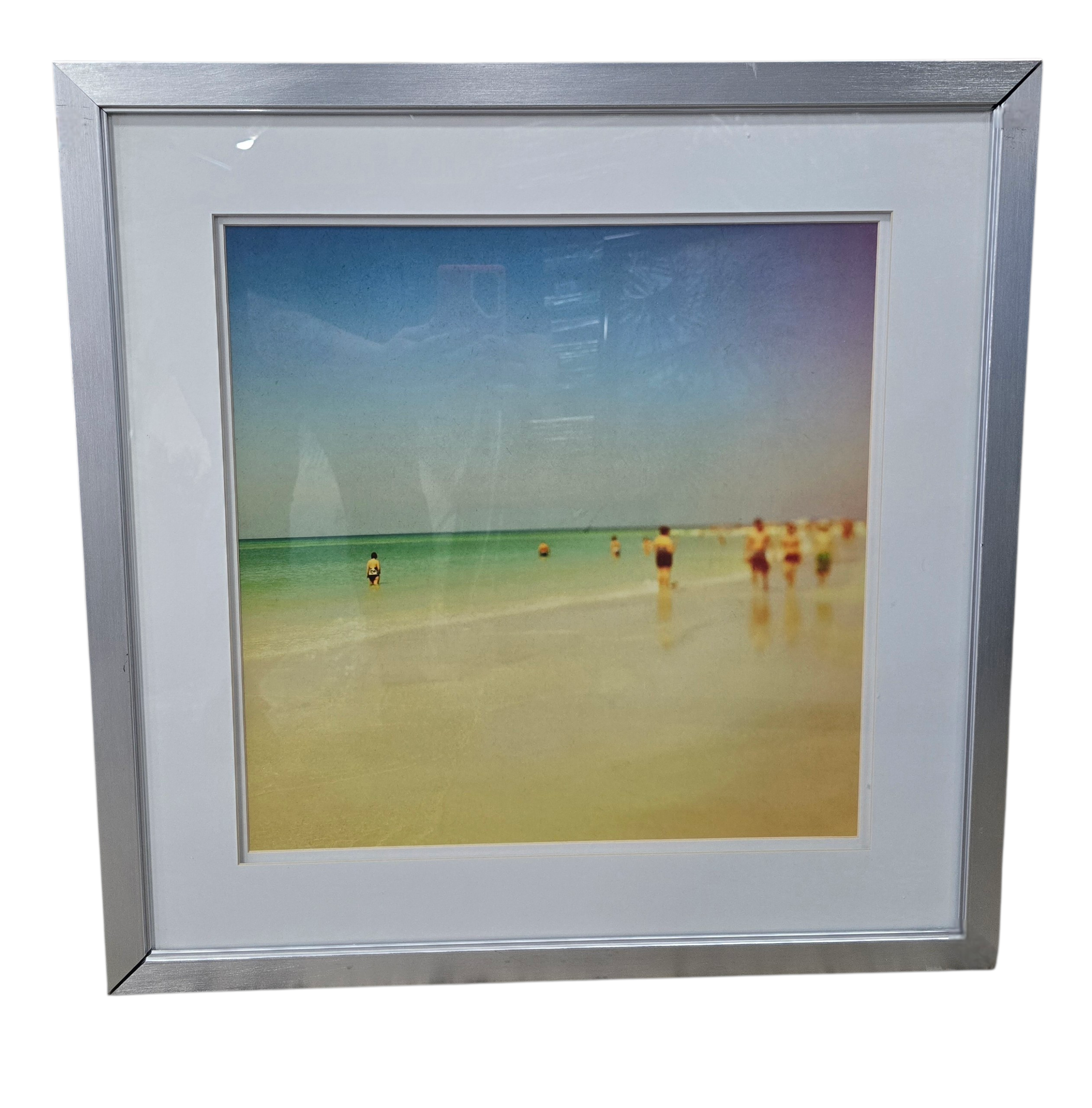 Framed coastal beach scene art with silver frame measuring 24.25 x 24.25 inches, used and in good condition