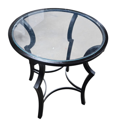 SHL used round glass top accent table featuring clear glass surface and curved black metal base sourced from an upscale resort