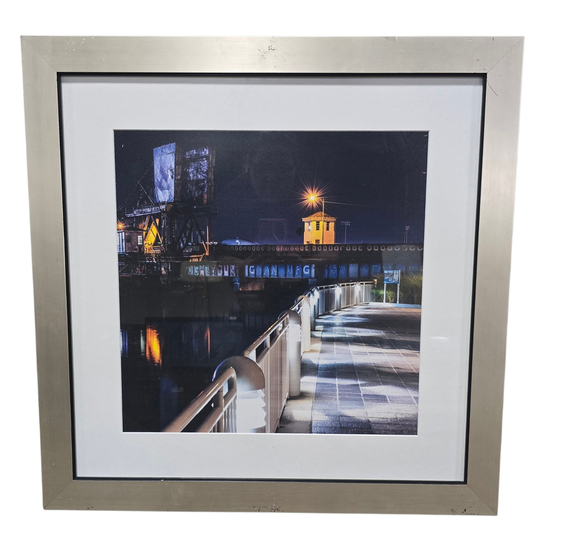 SHL framed nighttime waterfront cityscape wall art featuring illuminated boardwalk and harbor bridge scene measuring 27.5 x 27.5 used in good condition