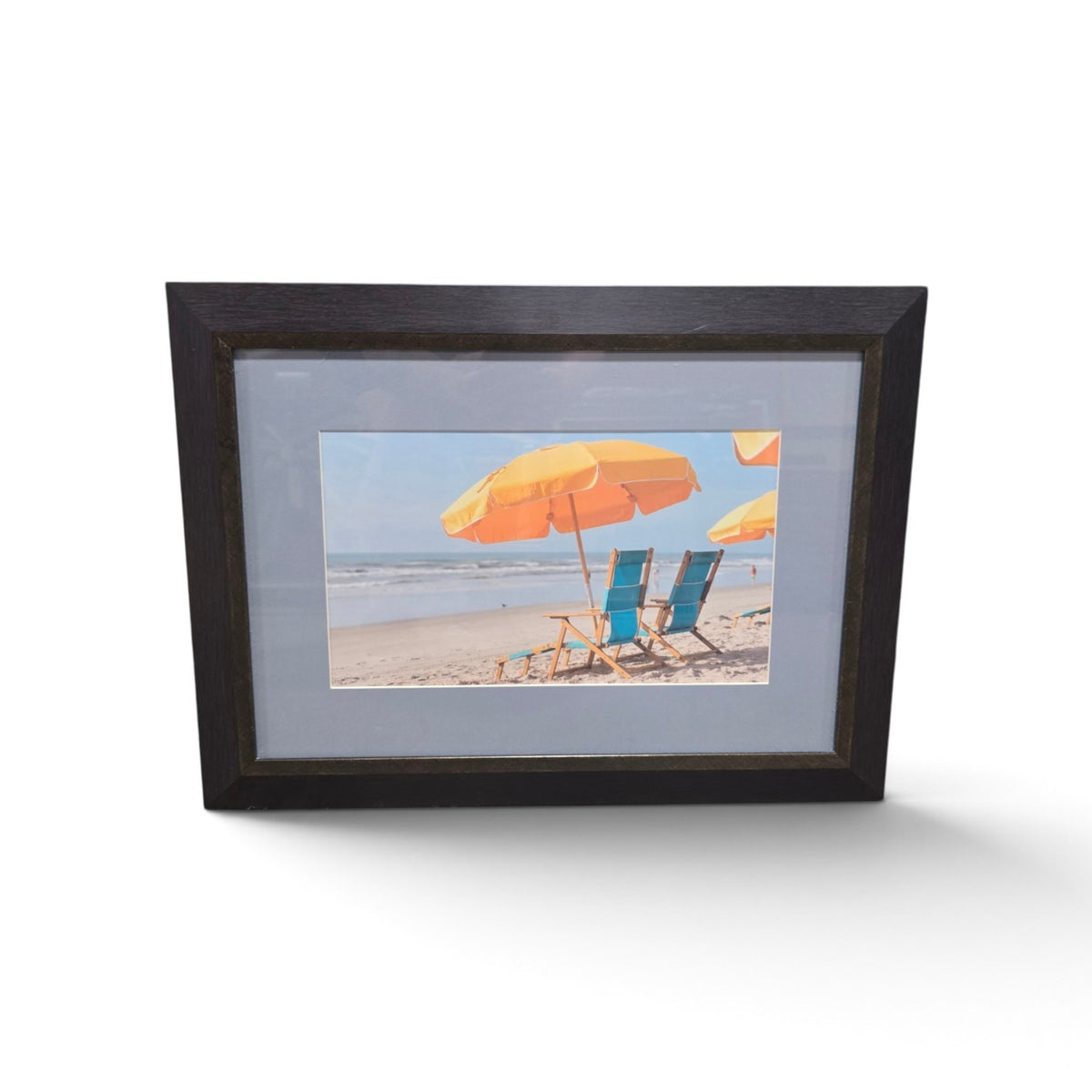 Framed beach photograph with colorful umbrellas and blue chairs overlooking the ocean