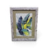 Framed tropical botanical artwork with blue green and yellow leaves and distressed whitewashed frame