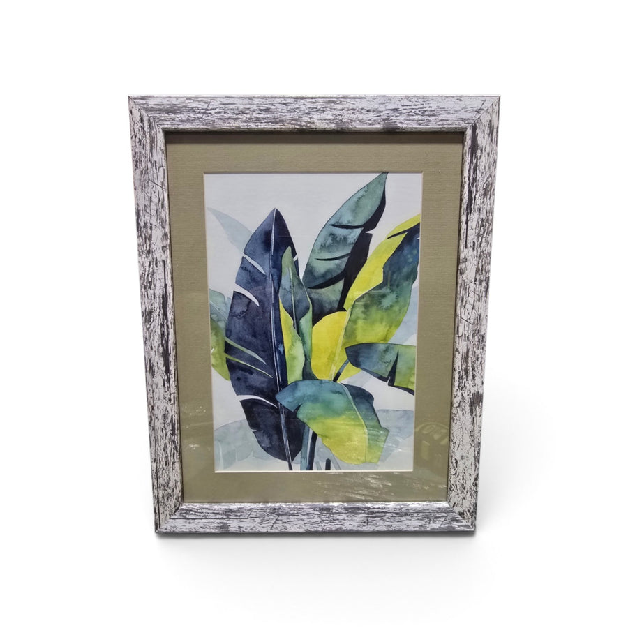 Framed tropical botanical artwork with blue green and yellow leaves and distressed whitewashed frame