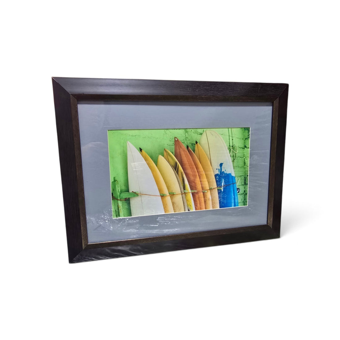Framed coastal photograph of colorful surfboards with green background and dark wood-look frame