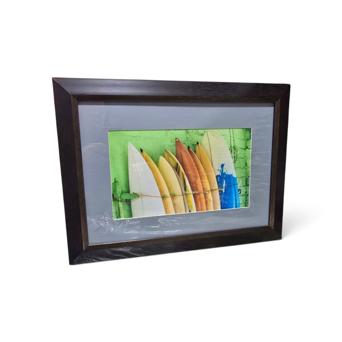 Framed coastal photograph of colorful surfboards with green background and dark wood-look frame